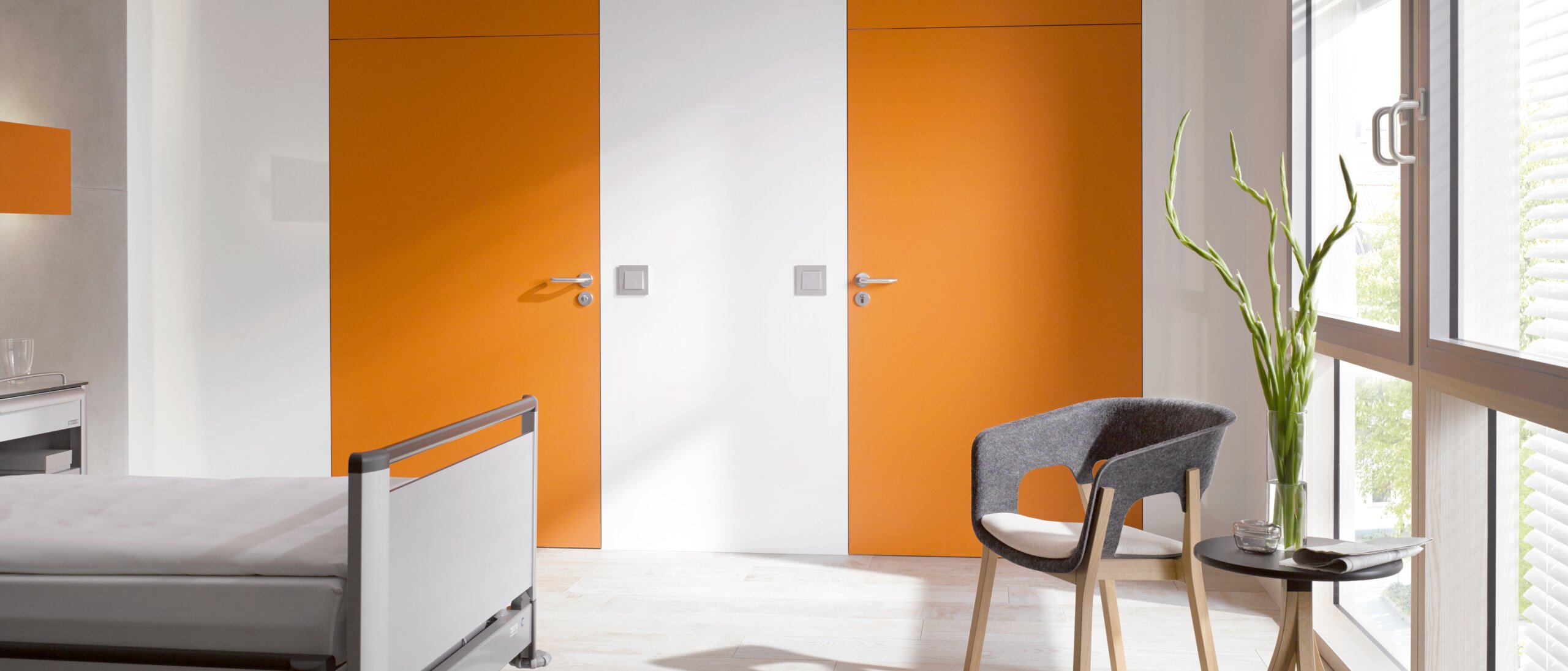 Chambre d'hôpital blanche avec deux portes orange équipées d'une poignée de porte en polyamide de couleur grise